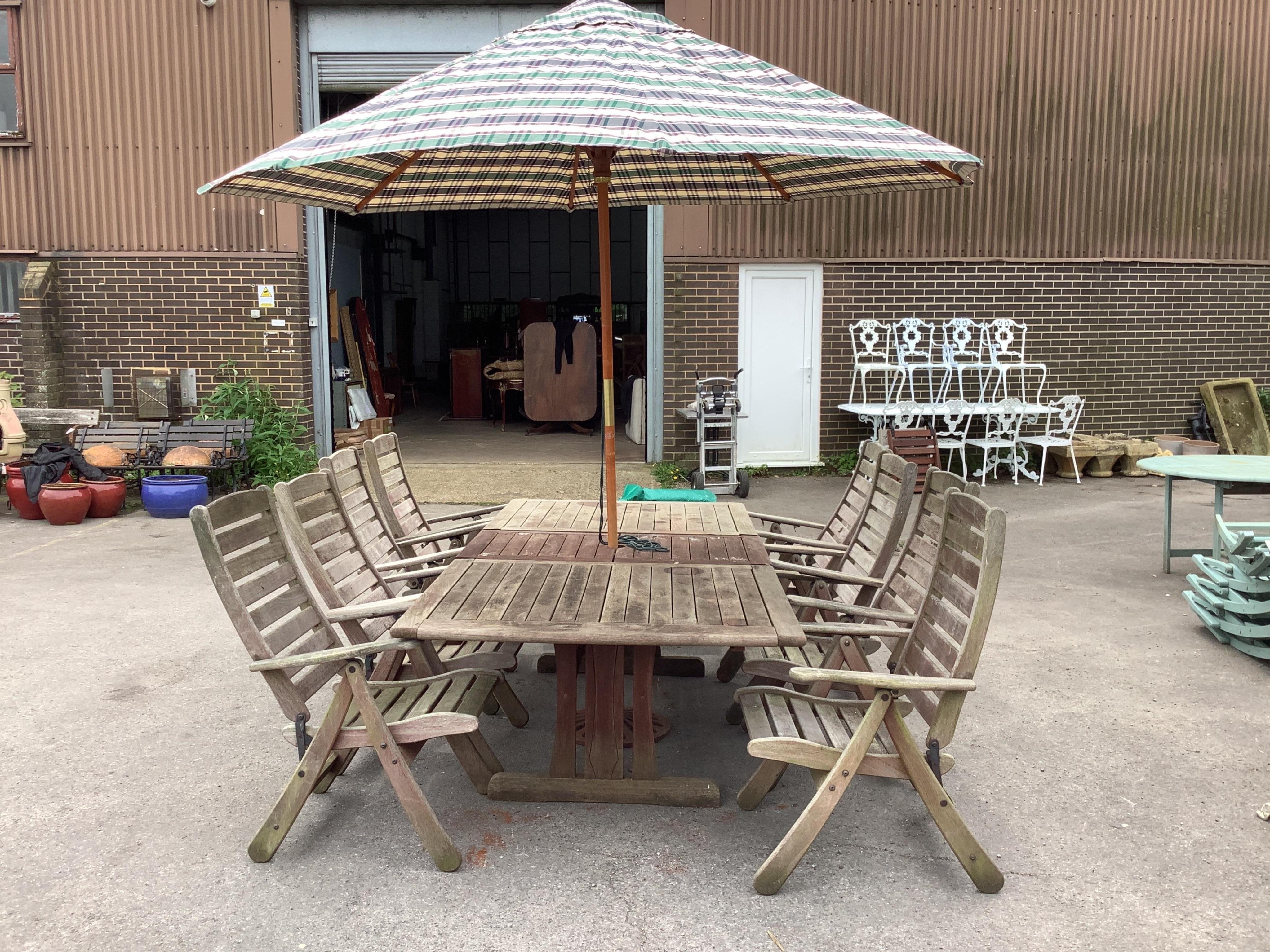 A large rectangular weathered teak extending garden table, width 256cm extended, depth 116cm, height 72cm together with a set of eight teak 'Clarecraft' elbow chairs, two with extending footrests, parasol, cast metal par